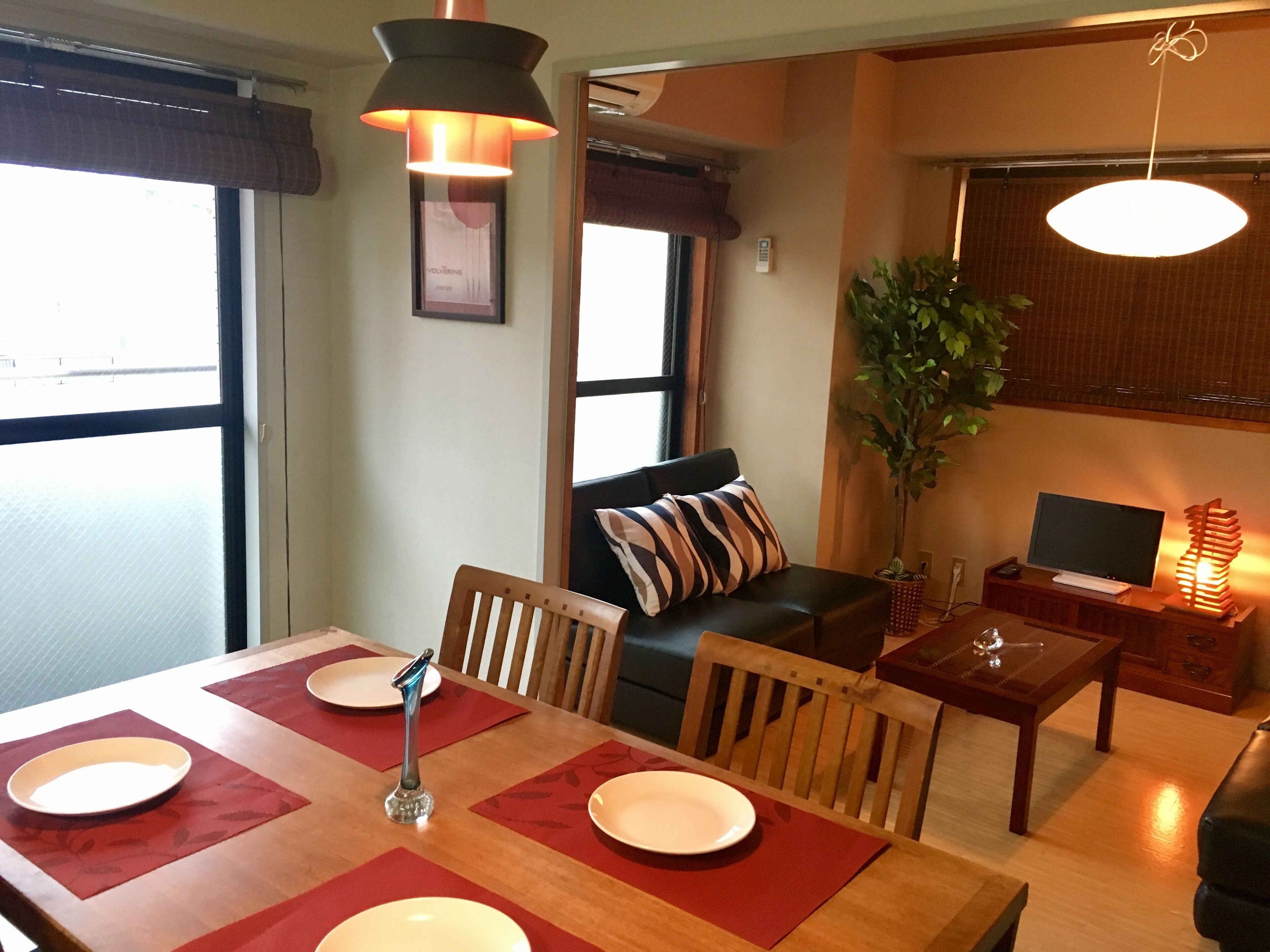 Un'area pranzo con un tavolo di legno, sedie e un sottopiatti rosso. C'è un divano con cuscini a righe e una pianta nell'angolo.