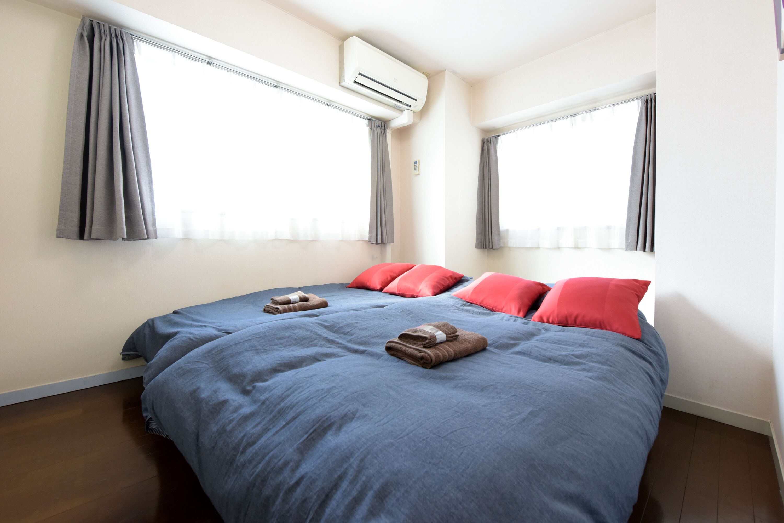 A bedroom with a large bed, grey curtains, red pillows, and an air conditioning unit.