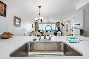Cozinha moderna com pia de aço inoxidável, um candelabro e vista para a sala de estar.