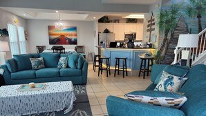 A living room with teal sofas, a coffee table, and a painting of a sunset over a pier.