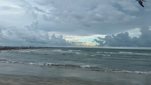 A beach with waves, a rocky shoreline, and a cloudy sky.