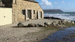 A stone building with a sloped roof, a wooden door, and windows with shutters. - In an exceptional position right on the beach is this spacious and comfortable cottage - a perfect g (Truro)