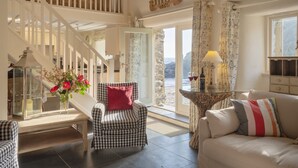 A spacious living area with a staircase, a checkered armchair, a sofa, and a view of the outdoors. - In an exceptional position right on the beach is this spacious and comfortable cottage - a perfect g (Truro)