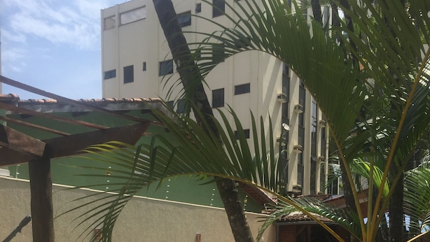 A swimming pool with a tiled deck, surrounded by palm trees and a building in the background. - BEAUTIFUL HOUSE WITH AN UNMISSABLE OUTDOOR AREA!!!! (Balneario Guarujá)