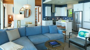 Un salon moderne avec un canapé bleu, une table basse et un fauteuil agrémenté d’un coussin à motifs de poissons.
