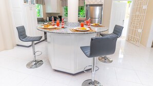 A modern kitchen with a central island, bar stools, and a refrigerator. - 4bd-4.bt~Ocean view ~Pool! Fully AC! Complimentary Breakfast!  (Sandy Bay)