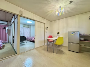 Een knus woongedeelte met kitchenette, een eethoek met tafel en stoelen, een bed met beddengoed met een patroon, en een schuifdeur naar een andere kamer.