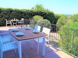 A patio with a wooden table set for four, white chairs, and a metal railing.