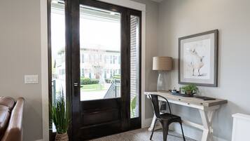 Un hall d’entrée moderne avec une porte en bois foncé, une console blanche surmontée d’une lampe, un tableau encadré et une plante en pot.