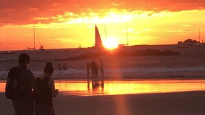Eine Strandansicht mit Segelbooten und Menschen im Abendrot.