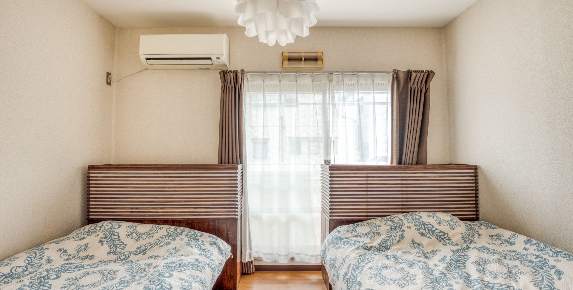 Ein Zimmer mit zwei Betten, einem Vorhangfenster, einer Klimaanlage und einer Deckenleuchte.