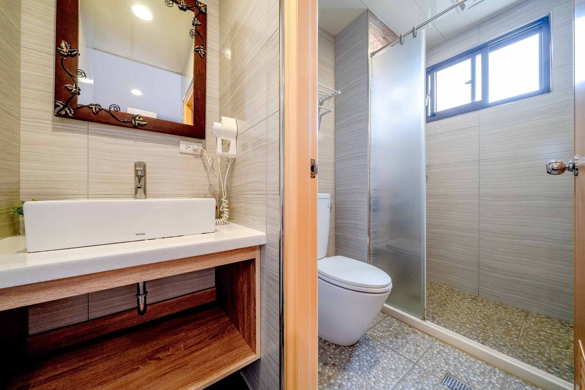 A modern bathroom with a white sink, a mirror with a decorative frame, a toilet, and a glass-enclosed shower area.