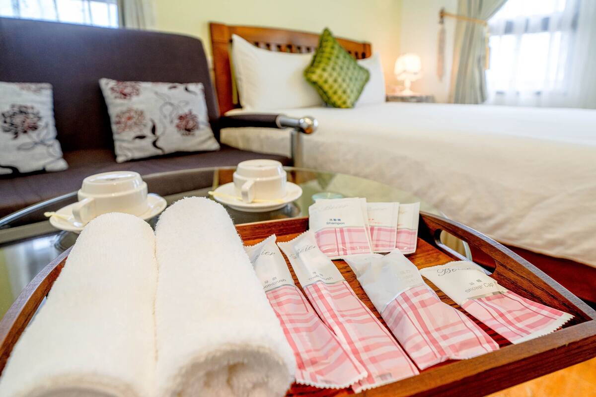 A hotel room with a bed, a sofa, and a tray with towels and toiletries.