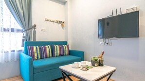 A room with a teal sofa, a small table with cups and a plant, a mounted TV, and a window with curtains. - Aurora Castle (Luodong)