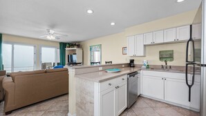 A modern kitchen with white cabinets, a stainless steel refrigerator, and a beige countertop. - Crystal Sands #101B * Beach Chair Set Included * Salt Water Vacations (Destin)
