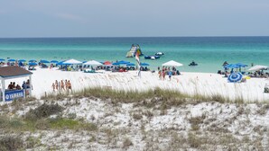 A beach with umbrellas, beach chairs, and a lifeguard tower. - Crystal Sands #101B * Beach Chair Set Included * Salt Water Vacations (Destin)