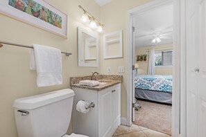 A bathroom with a toilet, sink, and mirrors. There is a towel hanging on a rack, and a painting above the sink. - Crystal Sands #101B * Beach Chair Set Included * DON'T MISS FALL BREAK! (Destin)