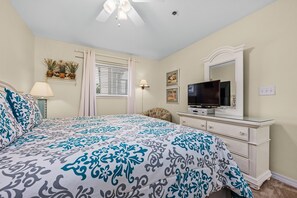 A bedroom with a bed, a TV, a dresser, a window with blinds, and a ceiling fan. - Crystal Sands #101B * Beach Chair Set Included * DON'T MISS FALL BREAK! (Destin)