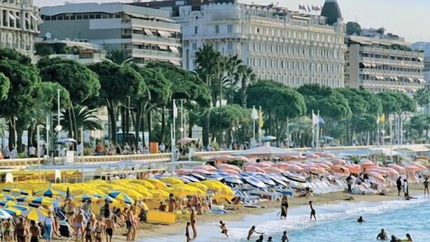 Une plage où l’on voit des gens nager et bronzer, des parasols et des bâtiments en arrière-plan.