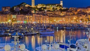 Un port de plaisance avec des bateaux amarrés, un bâtiment historique doté de tours et un paysage urbain avec des bâtiments illuminés.