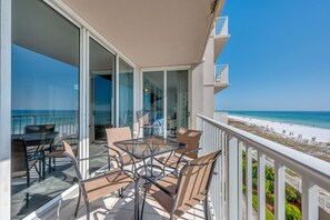 A balcony with a glass door leading to a room, a table with chairs, and a view of the beach.