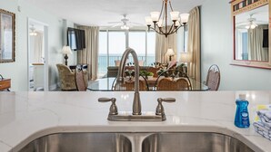 A modern kitchen with a stainless steel sink, a chandelier, and a dining area with wicker furniture. - Island Princess 416 * Gulf front~Beach Chair Set Included * Salt Water Vacations (Fort Walton Beach)