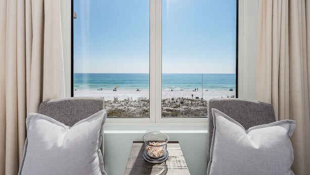 A room with a large window overlooking a beach, two chairs, and a small table with a decorative item. - Island Princess 416 * Gulf front~Beach Chair Set Included * Salt Water Vacations (Fort Walton Beach)