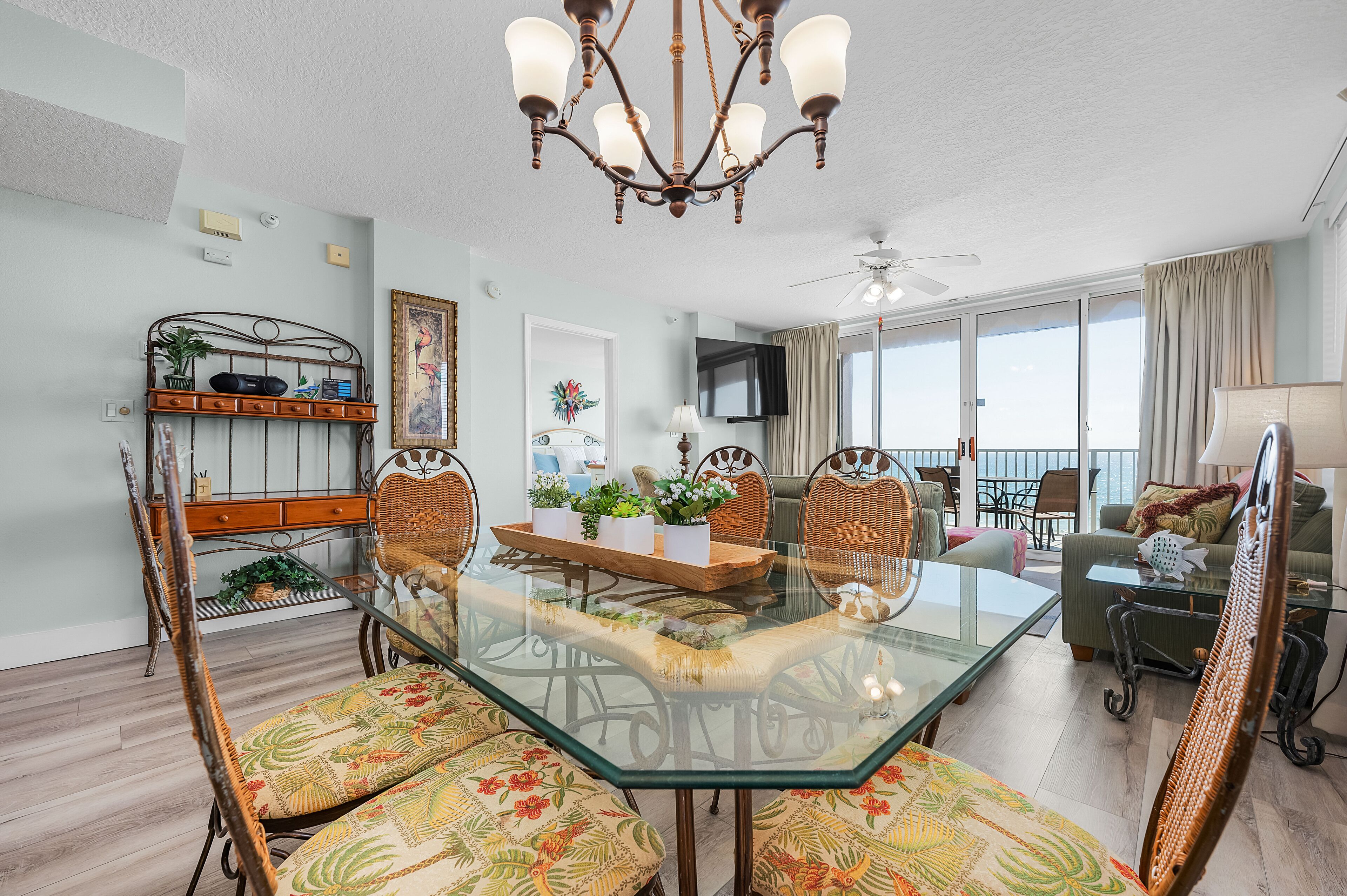 A dining area with a glass table, wicker chairs, and a chandelier.