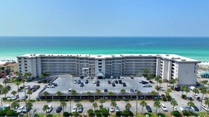 A hotel with a parking lot, multiple floors, and a view of the ocean.