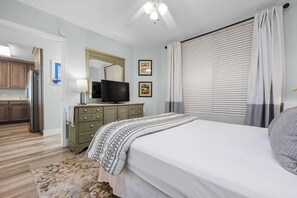 A bedroom with a bed, a dresser, a television, and a window with blinds.