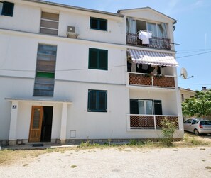 A multi-story building with balconies, a satellite dish, and a car parked nearby.