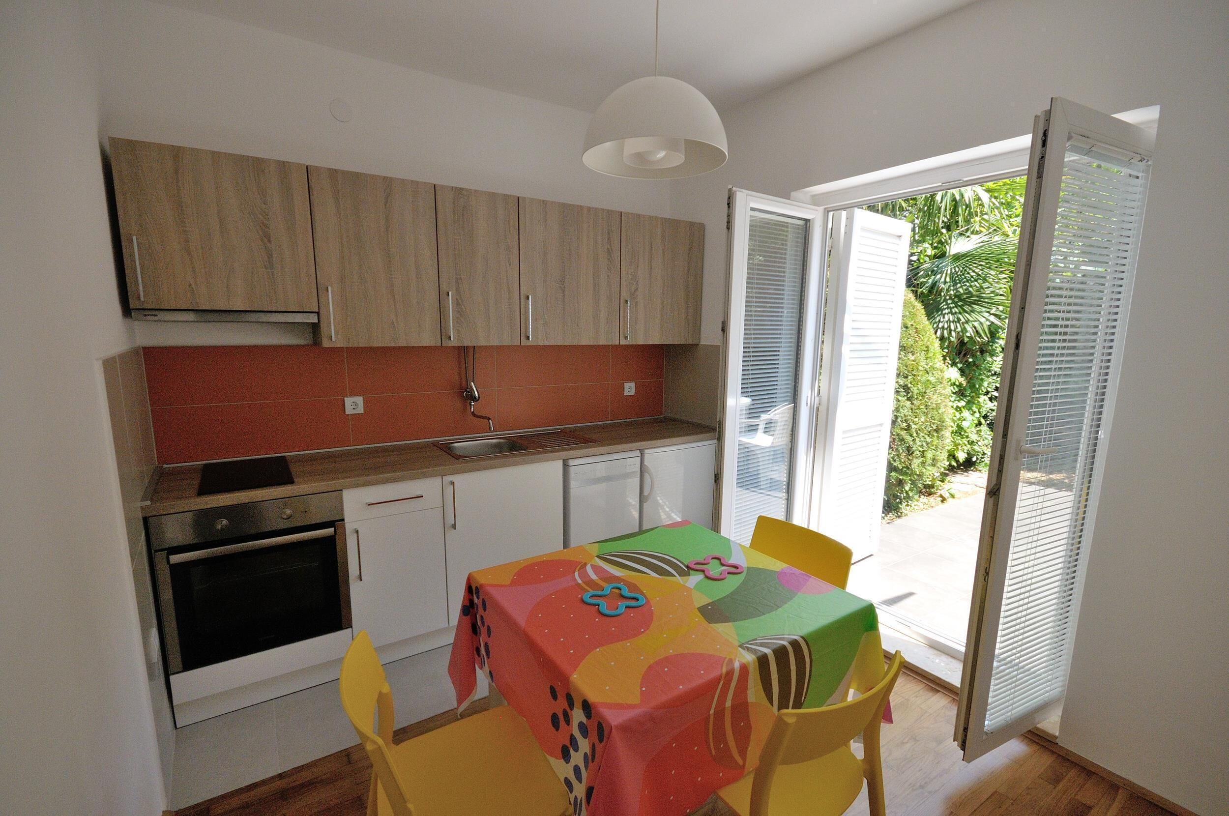 A compact kitchen with wooden cabinets, a built-in oven, and a dining area with a colorful tablecloth.