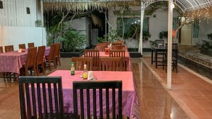 Restaurante com várias mesas e cadeiras, ventiladores de teto e plantas em vasos.