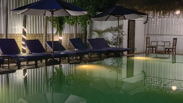 Piscina com espreguiçadeiras e guarda-sóis, cercada por uma vedação de bambu e plantas.