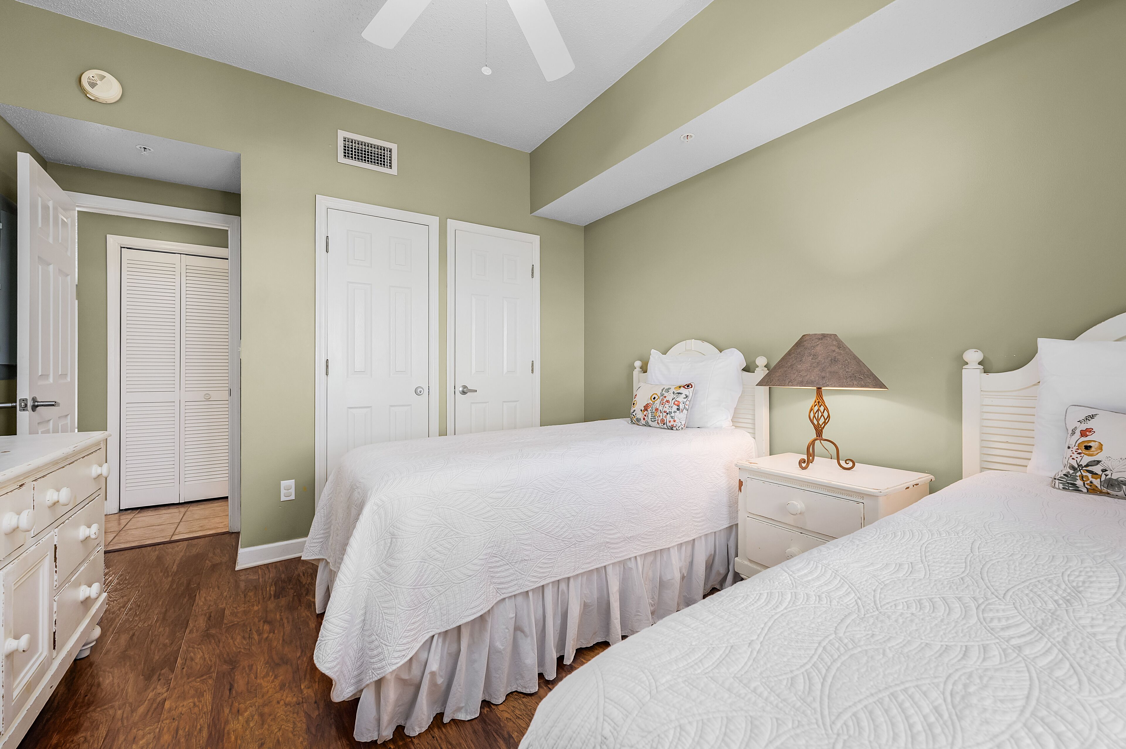 Une chambre avec deux lits, des meubles blancs et un ventilateur de plafond.