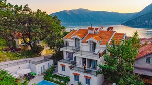 Ein mehrstöckiges Gebäude mit Swimmingpool, umgeben von Bäumen und mit Blick auf einen See mit Bergen im Hintergrund.