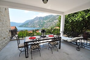 Un balcon avec une table et des chaises, une chaise longue et une vue sur un lac et des montagnes.