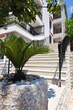 A multi-story building with a stone facade, a palm tree in a planter, and a staircase with black railings. - Castello Risano (Risan)