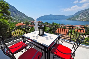 Un balcon avec une table et des chaises rouges, donnant sur un lac et des montagnes.