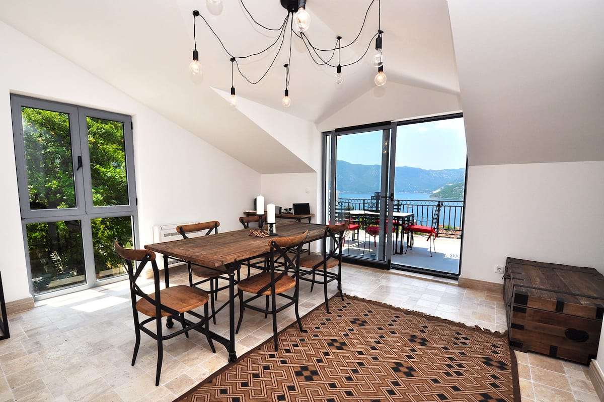 Un amplio comedor con una mesa y sillas de madera, una araña y vistas al exterior.