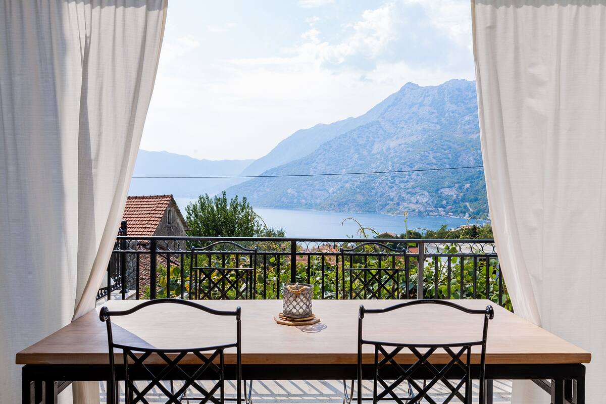 Un balcón con una mesa de madera y dos sillas, con vistas a un paisaje montañoso y un lago.