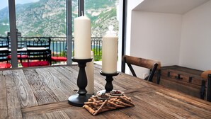 Ein Holztisch mit zwei Kerzen und einer Schale mit Snacks, mit Blick auf eine gebirgige Landschaft durch große Fenster.