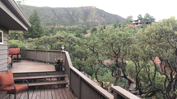 Eine Holzterrasse mit Gartenmöbeln, mit Blick auf eine gebirgige Landschaft mit Bäumen.