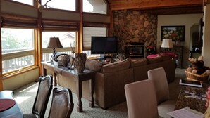 Ein gemütliches Wohnzimmer mit Kamin aus Stein, einem Fernseher und einem Essbereich mit Stühlen und Tisch.