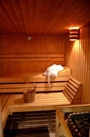A wooden sauna with benches, a wooden bucket, and a heater. - Hotel Vierenstraße (Sehmatal)