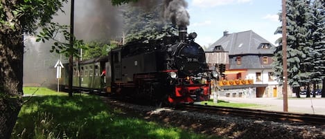 A steam locomotive with the number 99786 on a railway track surrounded by greenery and a building with a sloped roof.