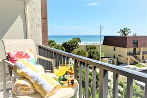 Un balcon avec vue sur la plage, une table avec une serviette, une boisson et une bouteille de Corona Extra.
