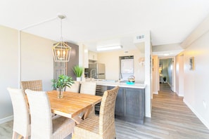 A modern kitchen with a central island, a dining area with wicker chairs, and a hallway leading to other rooms.