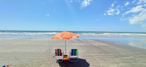 Ein Strand mit zwei Liegen unter einem orangefarbenen Sonnenschirm.