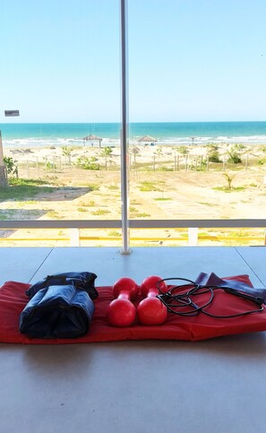 Ein Zimmer mit Blick auf den Strand, eine rote Matte mit Fitnessgeräten und ein Fenster mit einem Metallstab.